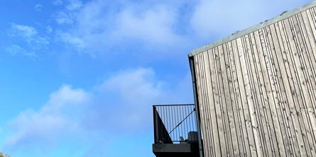 Billede af siden af et hus med en flot træfacade og en stål altan. 