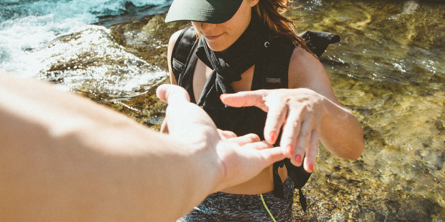 Unge pige bliver hjulpet op af nogle klipper på en strand - billede taget fra Unsplash.com